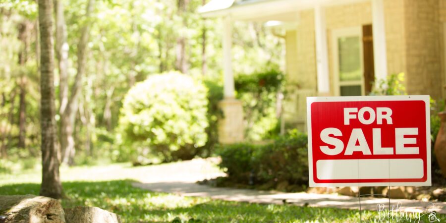 For sale sign in front of a new home on a sunny day.