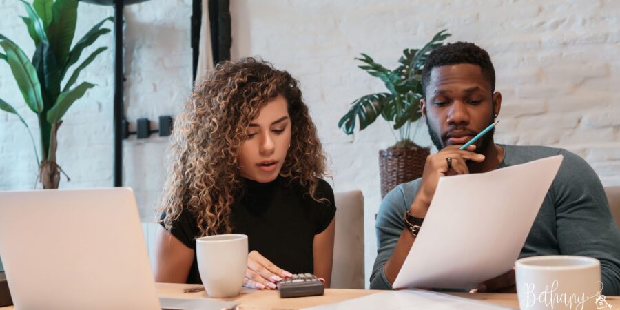 Happy couple reviewing their home budget with a calculator and coffee, preparing to buy a home in a rising market.